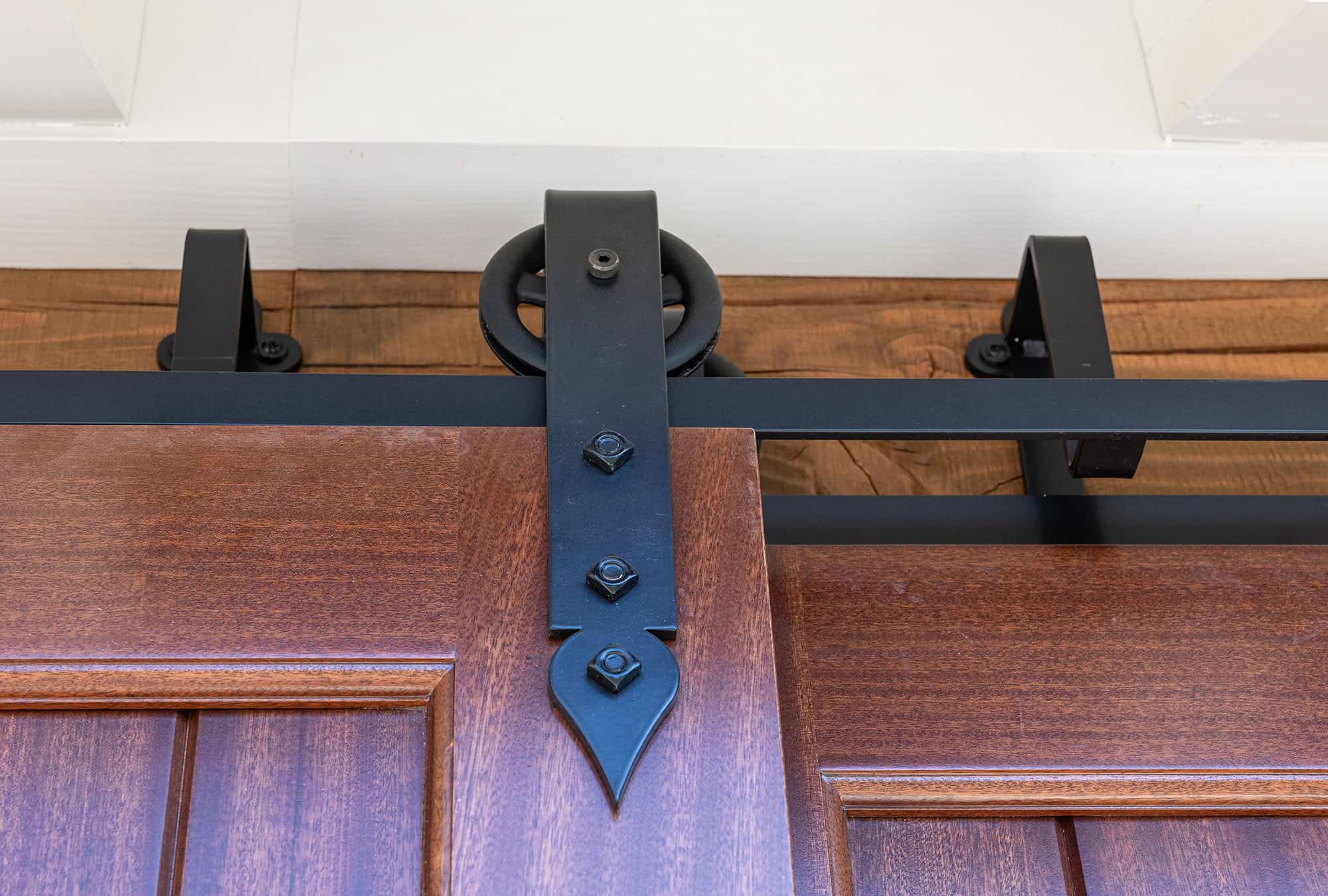 Close-up view of a sliding barn door system in a luxury horse barn, featuring the metal track, black hardware, and upper edge of a wooden door with decorative detailing.