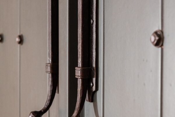 Close-up of two dark metal handles mounted vertically on a rustic, paneled wooden door—perfect for a luxury horse barn. Light is visible along the top edge of the door.