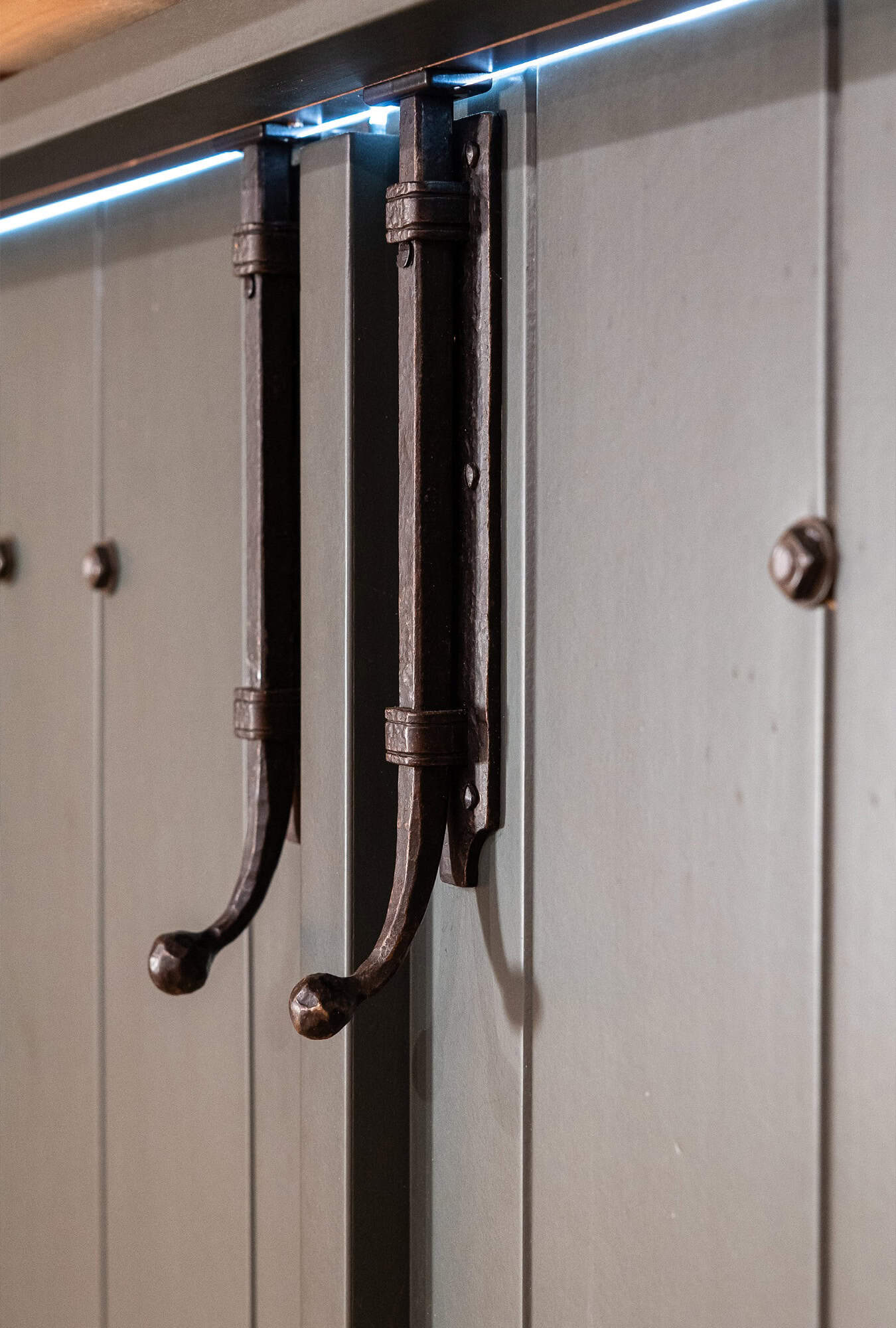 Close-up of two dark metal handles mounted vertically on a rustic, paneled wooden door—perfect for a luxury horse barn. Light is visible along the top edge of the door.