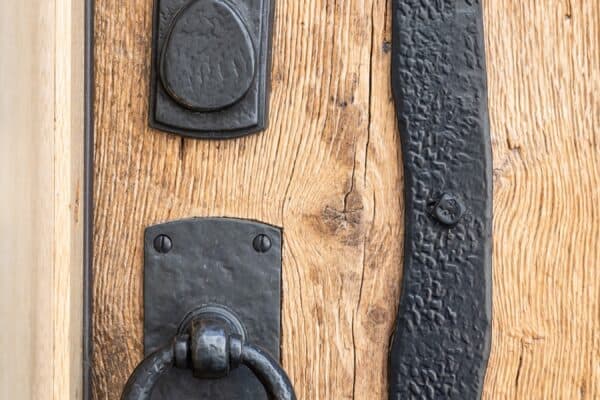 Close-up of a rustic wooden door with black wrought iron details, including a round door knocker and a decorative plate—an elegant touch perfect for a luxury horse barn or upscale party barn.
