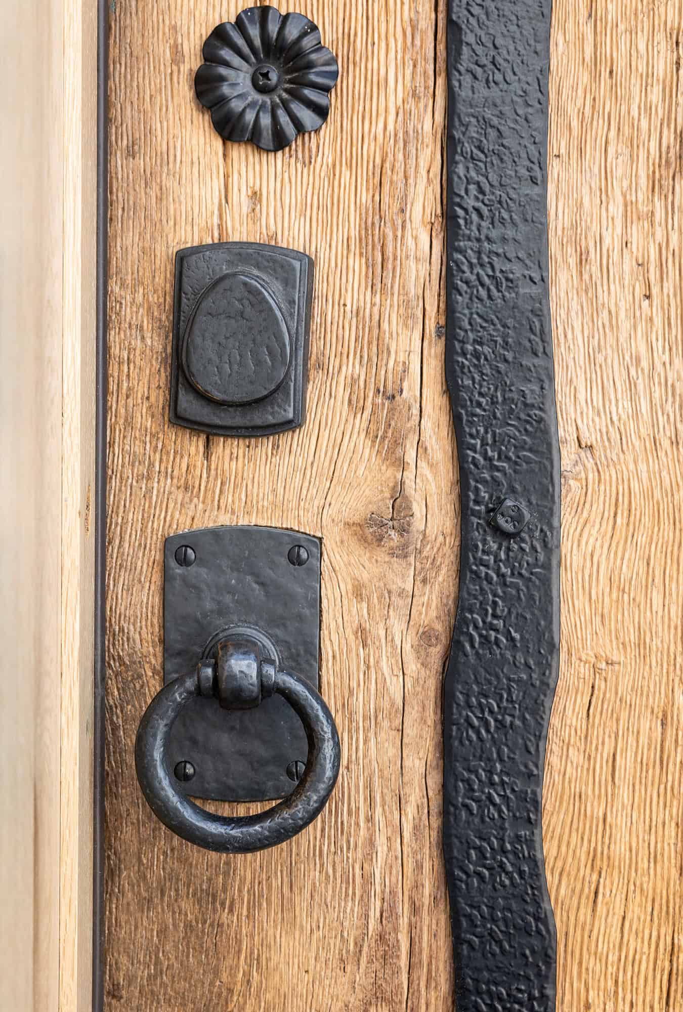 Close-up of a rustic wooden door with black wrought iron details, including a round door knocker and a decorative plate—an elegant touch perfect for a luxury horse barn or upscale party barn.