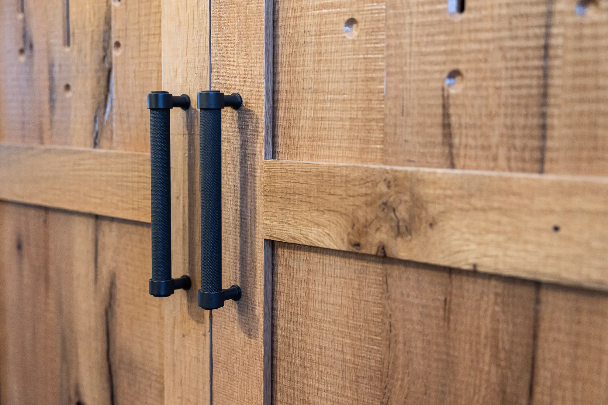 Close-up of two black metal handles on rustic wooden cabinet doors, showcasing visible wood grain and knots—perfect for adding authentic charm to a luxury horse barn or refined bank barn interior.