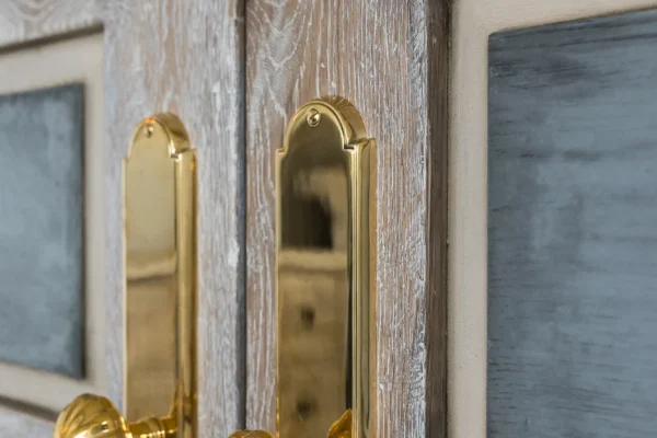 Close-up of a double wooden door with ornate gold handles and a gold bolt latch, perfect for a luxury horse barn. The doors have a weathered finish and frosted glass panels.
