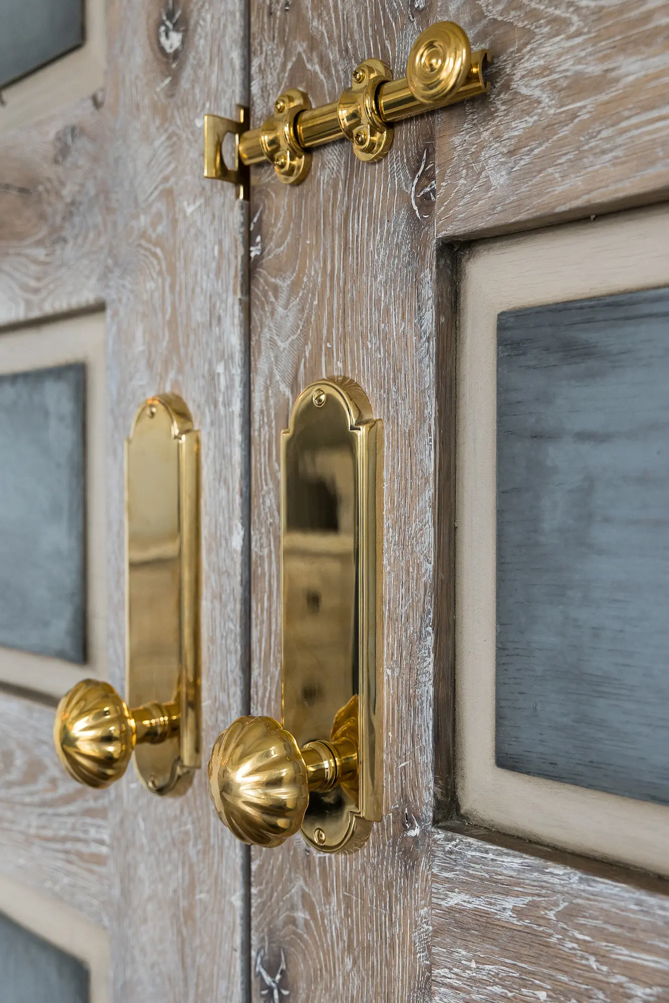 Close-up of a double wooden door with ornate gold handles and a gold bolt latch, perfect for a luxury horse barn. The doors have a weathered finish and frosted glass panels.