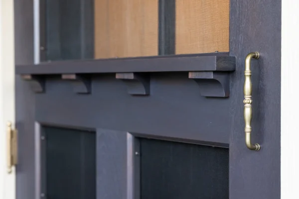 Close-up of a dark wooden door with decorative molding and a brass handle on the right side; part of the door's paneling and mesh screen are also visible in this elegant party barn setting.