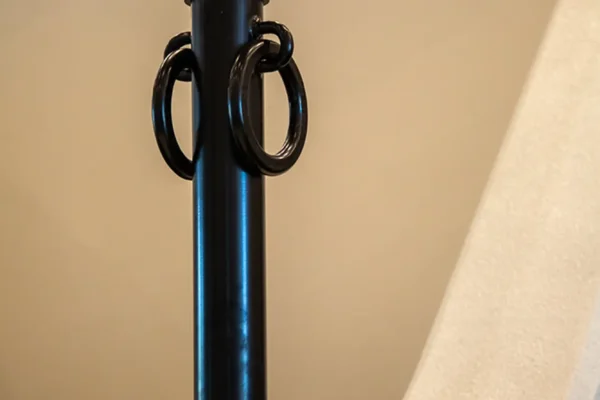 A black metal post with a shiny gold sphere on top and two large circular rings on each side, reminiscent of elegant decor often found in a luxury home, mounted on a light-colored surface against a plain background.